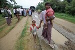 Seorang pria menggendong anaknya sementara warga berkumpul untuk menerima bantuan di sebuah kamp bagi warga Rohingya yang tergusur karena kekerasan baru-baru ini, di luar Sittwe, Myanmar, pada tanggal 15 Juni. Pada akhir bulan Agustus, Palang Merah Indonesia mengirim tujuh ton bantuan kemanusiaan kepada umat Muslim dan Budha di negara bagian Rakhine, Myanmar. [Soe Zeya Tun/Reuters]