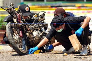 Police investigators collect evidence from the blast site, next to a damaged motorcycle used by a suicide bomber who attacked police headquarters in Poso, Sulawesi on June 3rd. Police believe the man was a member of an Islamist terror group affiliated with jailed extremist Abu Omar. [Olagondronk/AFP]