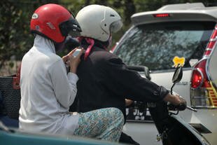 A woman uses her smartphone on the back of a motorcycle in Jakarta on October 19th, 2013. Smartphone app MataMassa enables residents of greater Jakarta to report campaign violations, such as improper placement of posters. [Bay Ismoyo/AFP]