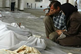 A Syrian couple mourns in front of bodies wrapped in shrouds following an alleged toxic gas attack by pro-Assad forces in eastern Ghouta, on the outskirts of Damascus on August 21st. The opposition says thousands, mostly women and children, died in a succession of chemical attacks launched by the regime. [AFP Photo/Shaam News]